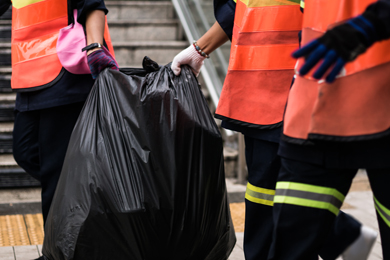 waste disposal workers are helping each other to transport garbage bags